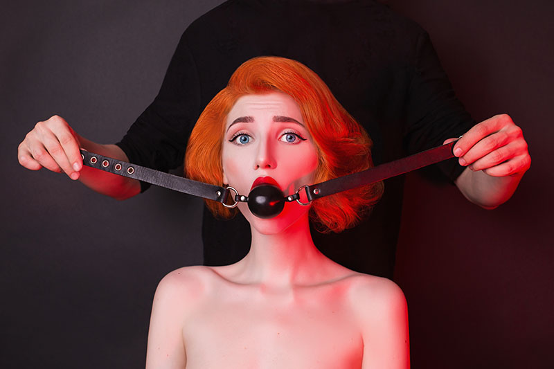 rothaarige Frau mit BDSM Spielzeug im Mund